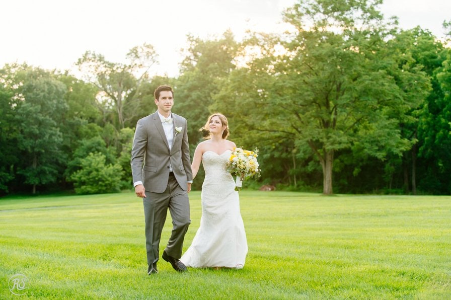 bride and groom walking through a green field 