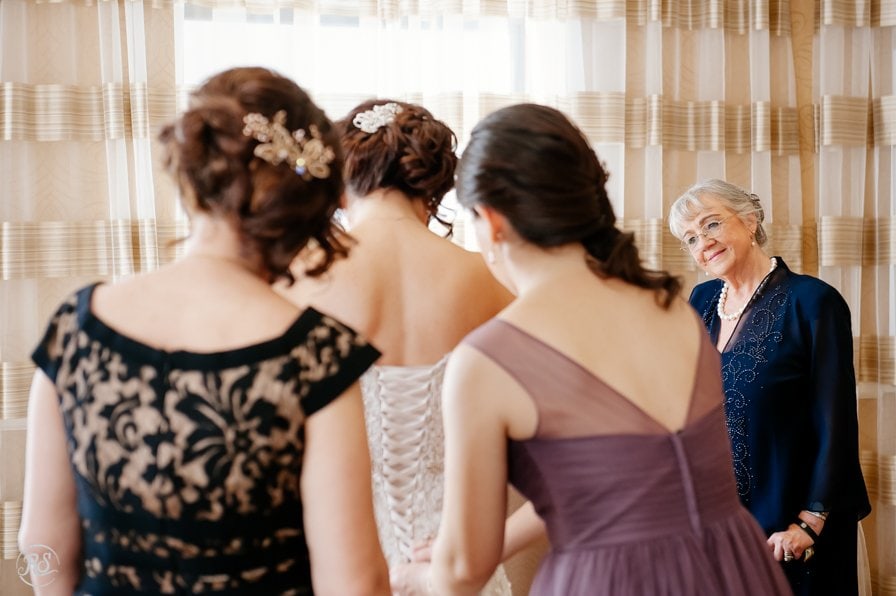 Mother of the bride and mother of the groom helping bride with wedding dress