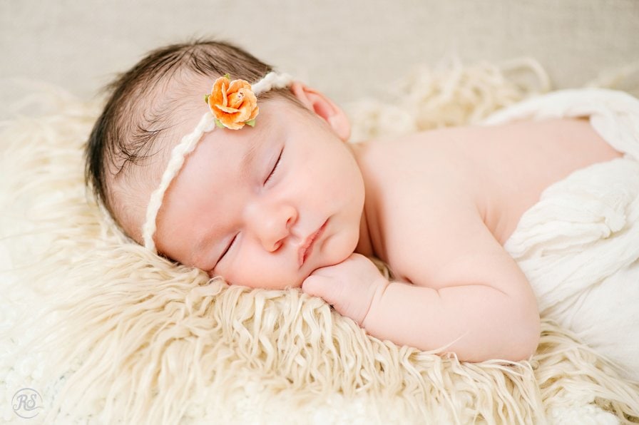 baby on fur blanket with white cheesecloth swaddle and peach flower headband 